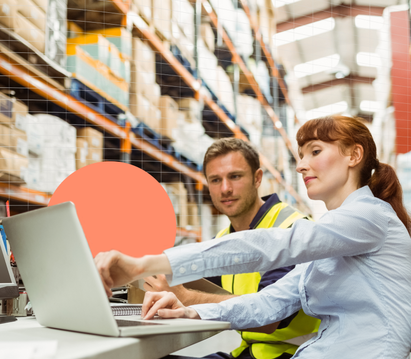 Two employees working together in the warehouse with an open laptop. 